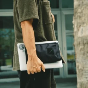 Tech pouch Evergoods CAP1 nero tenuto in mano insieme a un laptop per mostrare le dimensioni compatte.
