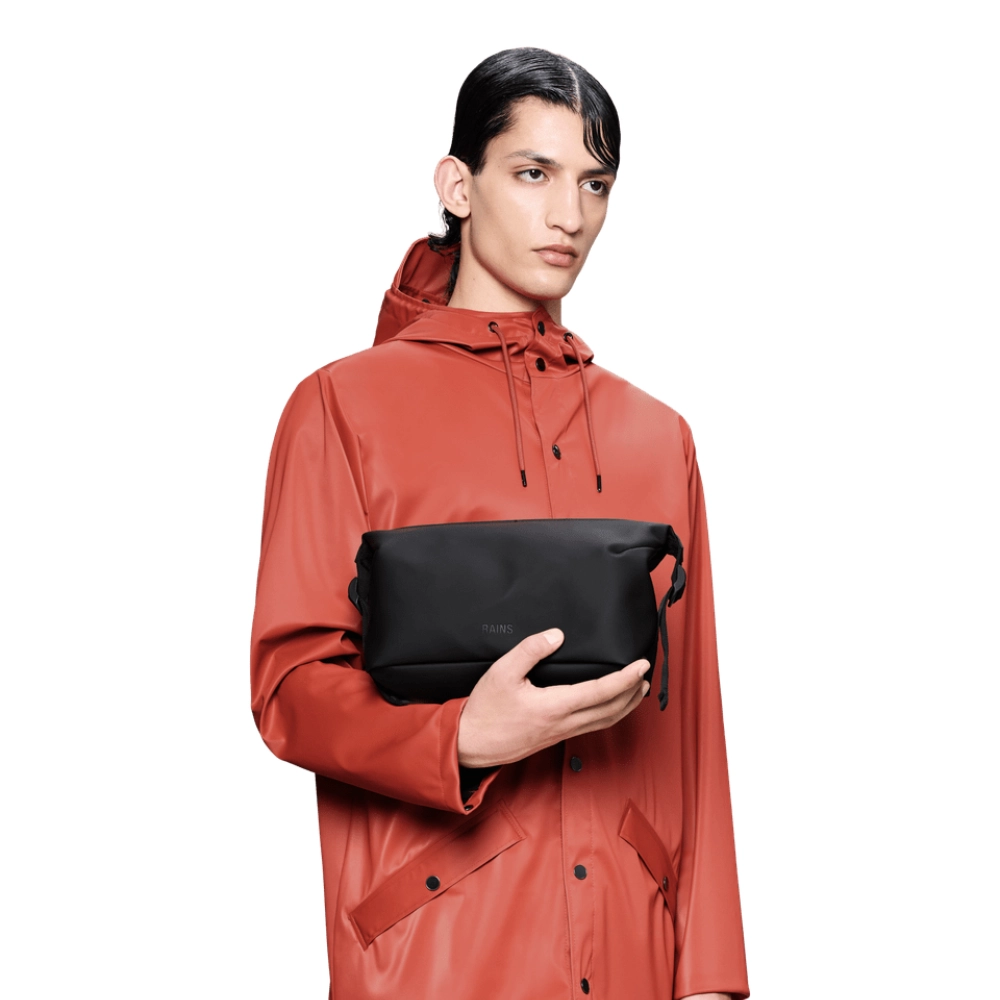 Uomo con beauty case Rains Hilo Wash Bag W4 nero abbinato a impermeabile rosso.