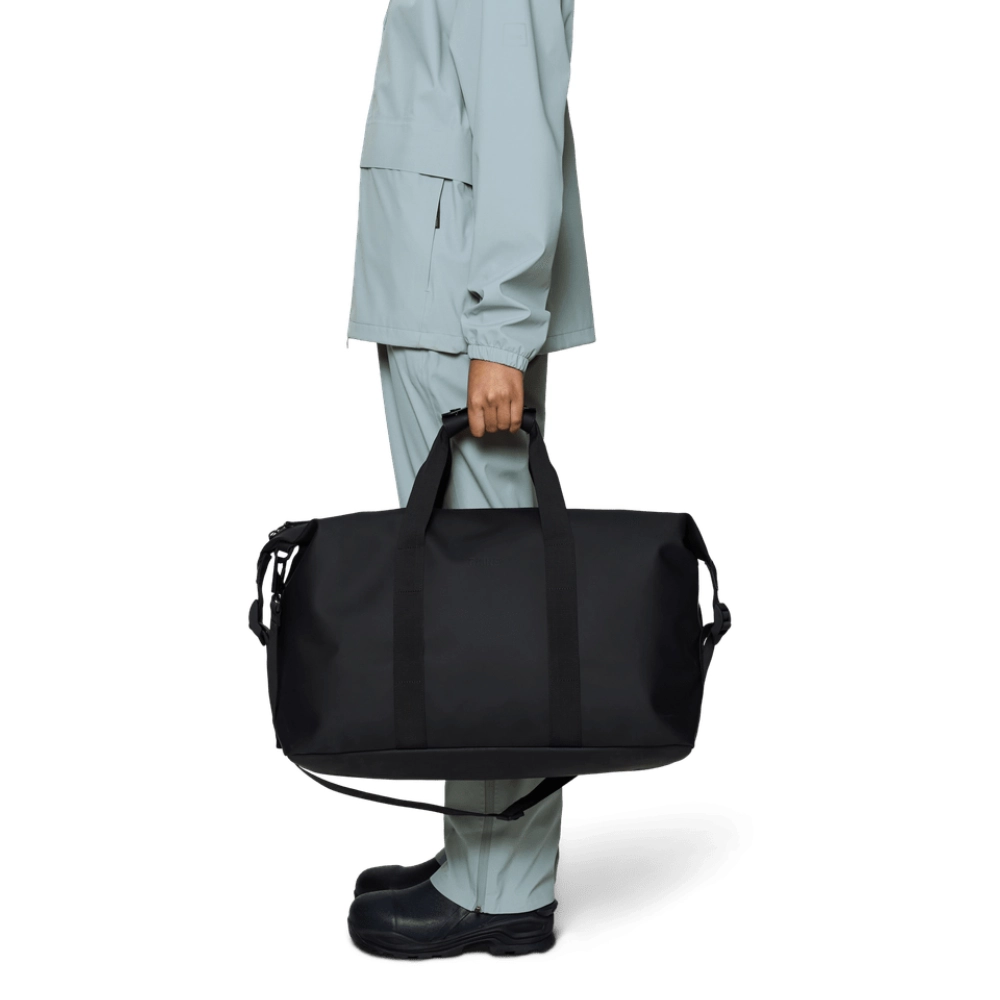 Modello che trasporta a mano il borsone Rains Hilo Weekend Bag W3 nero impermeabile da 38 litri.