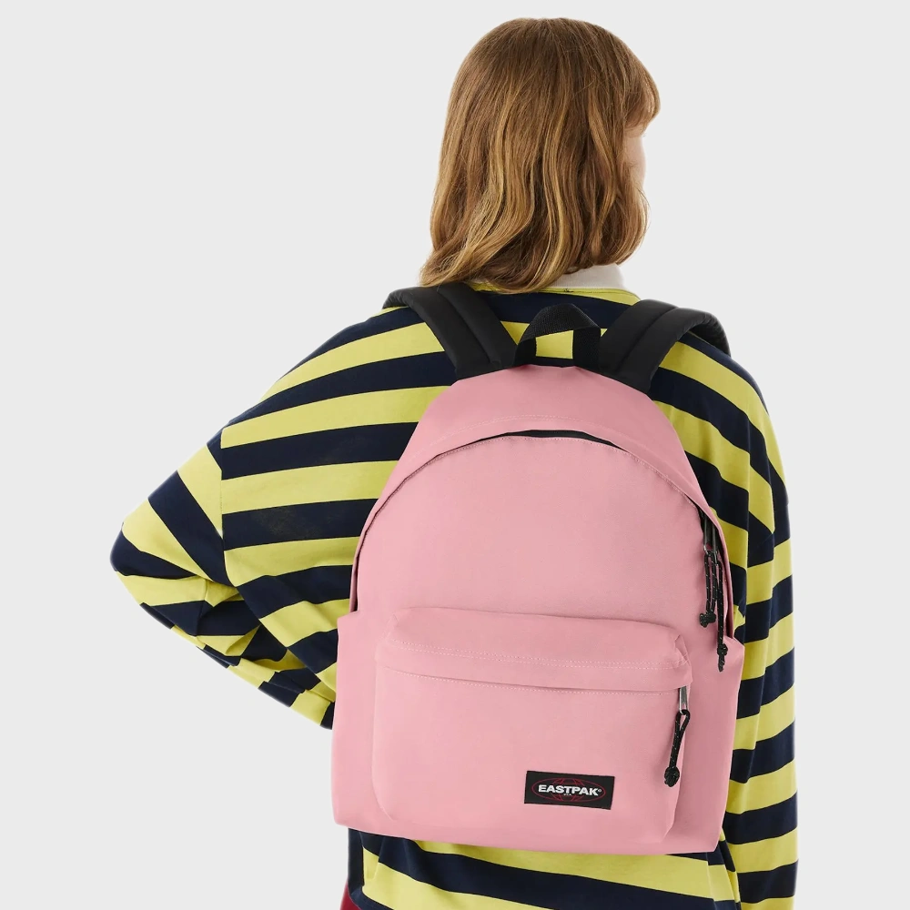 Zaino rosa confetto indossato a spalla sopra una maglia a righe gialle e nere.