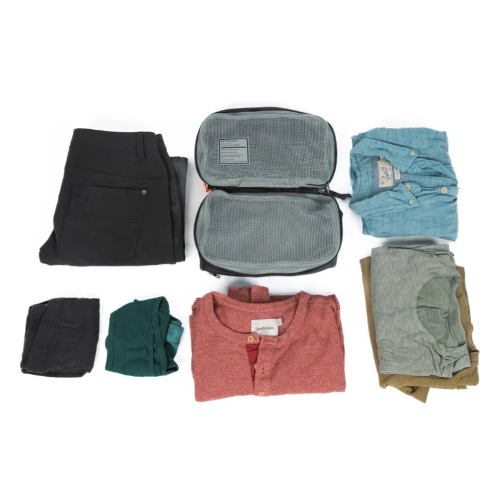 Organizzatore da viaggio aperto circondato da camicie, magliette e pantaloni piegati.